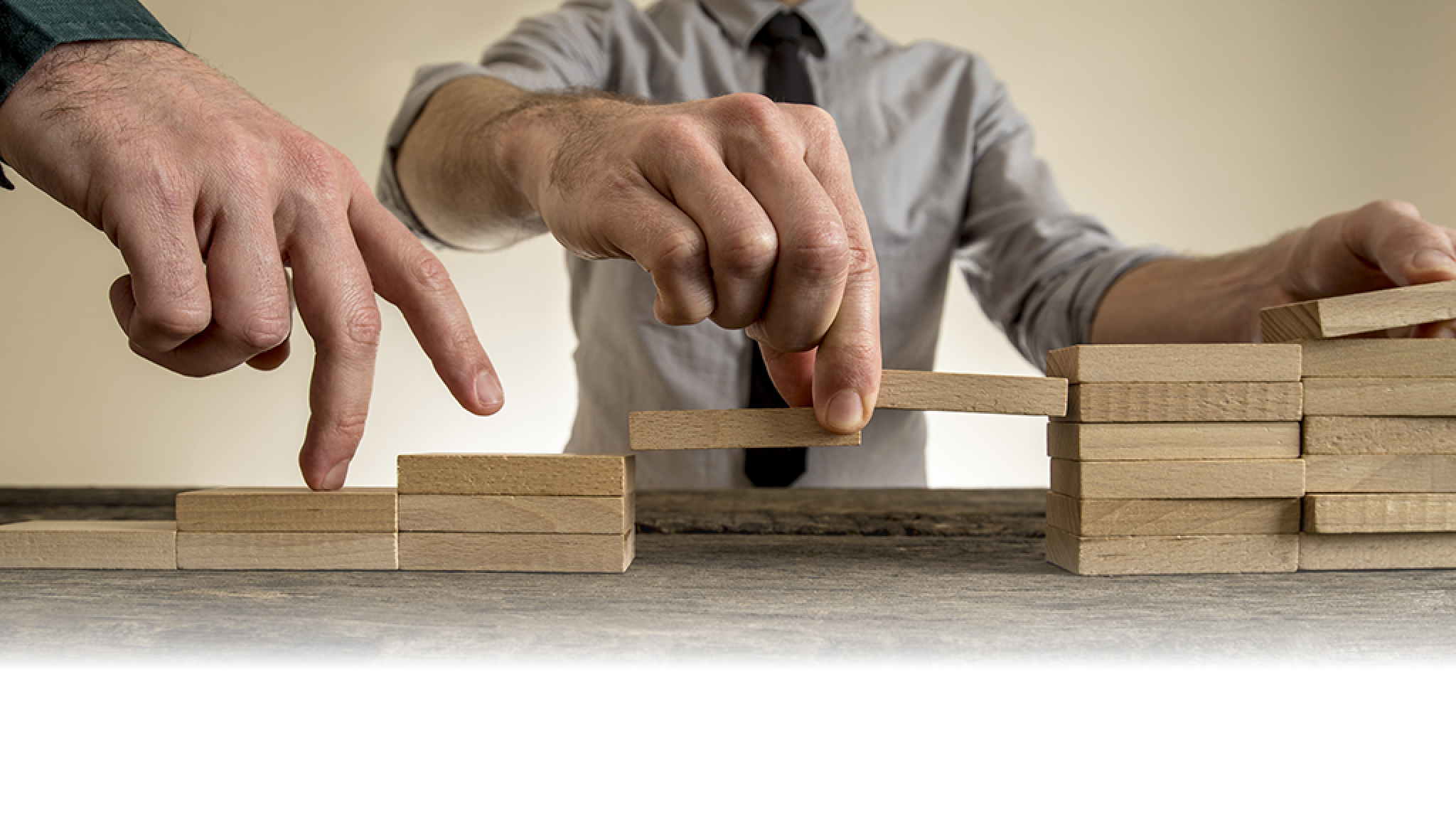 Businessman building staircase with wooden blocks to span a gap for partner to walk his fingers across towards promotion and progress.